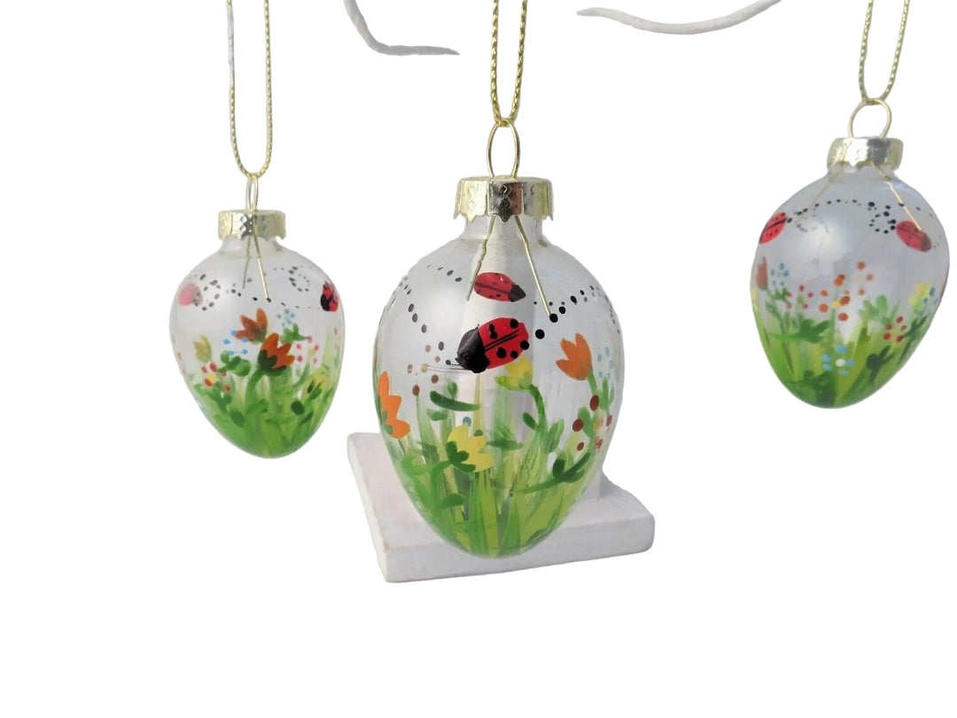 Decorative glass ornaments with floral and insect designs on a white stand.