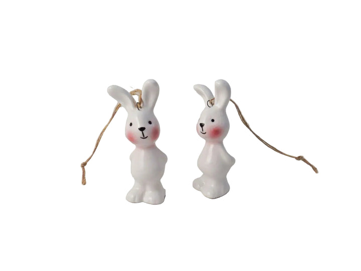 Two white ceramic bunny ornaments with pink accents on a light gray background