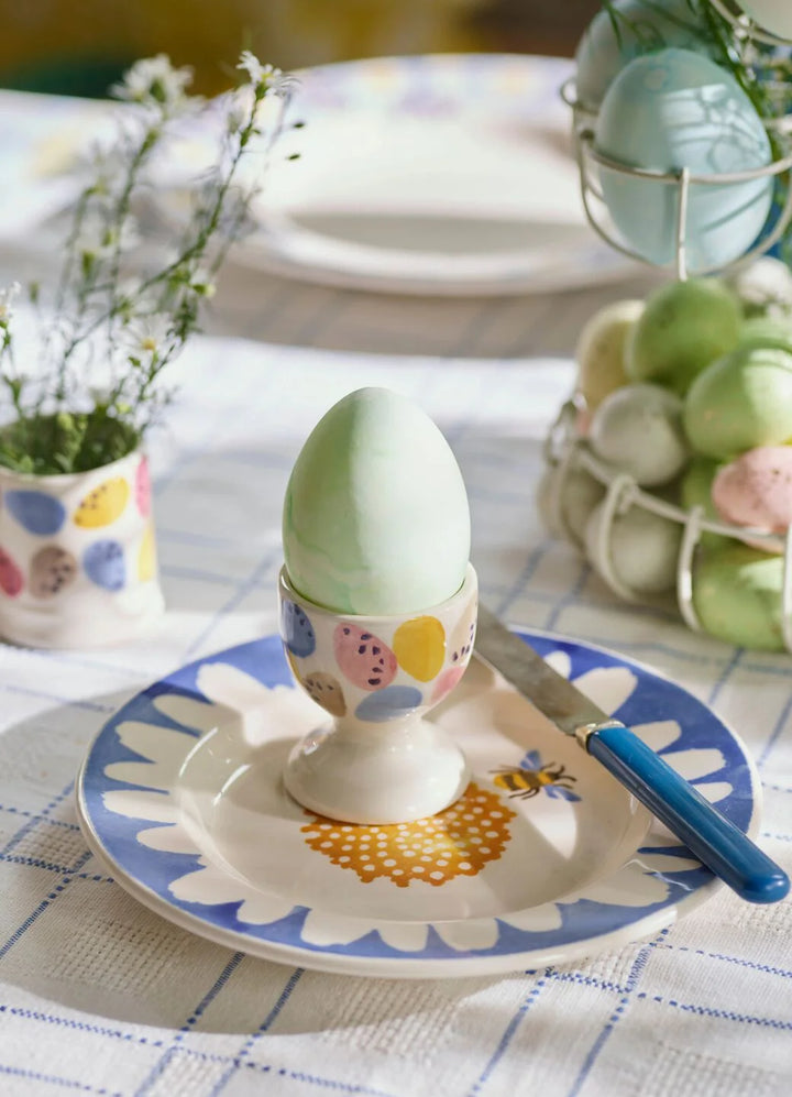Decorative Easter egg in a colorful holder on a table with a plate and knife.
