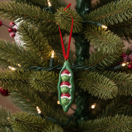 Decorative ornament shaped like a green pea pod with two smiling peas on a white background