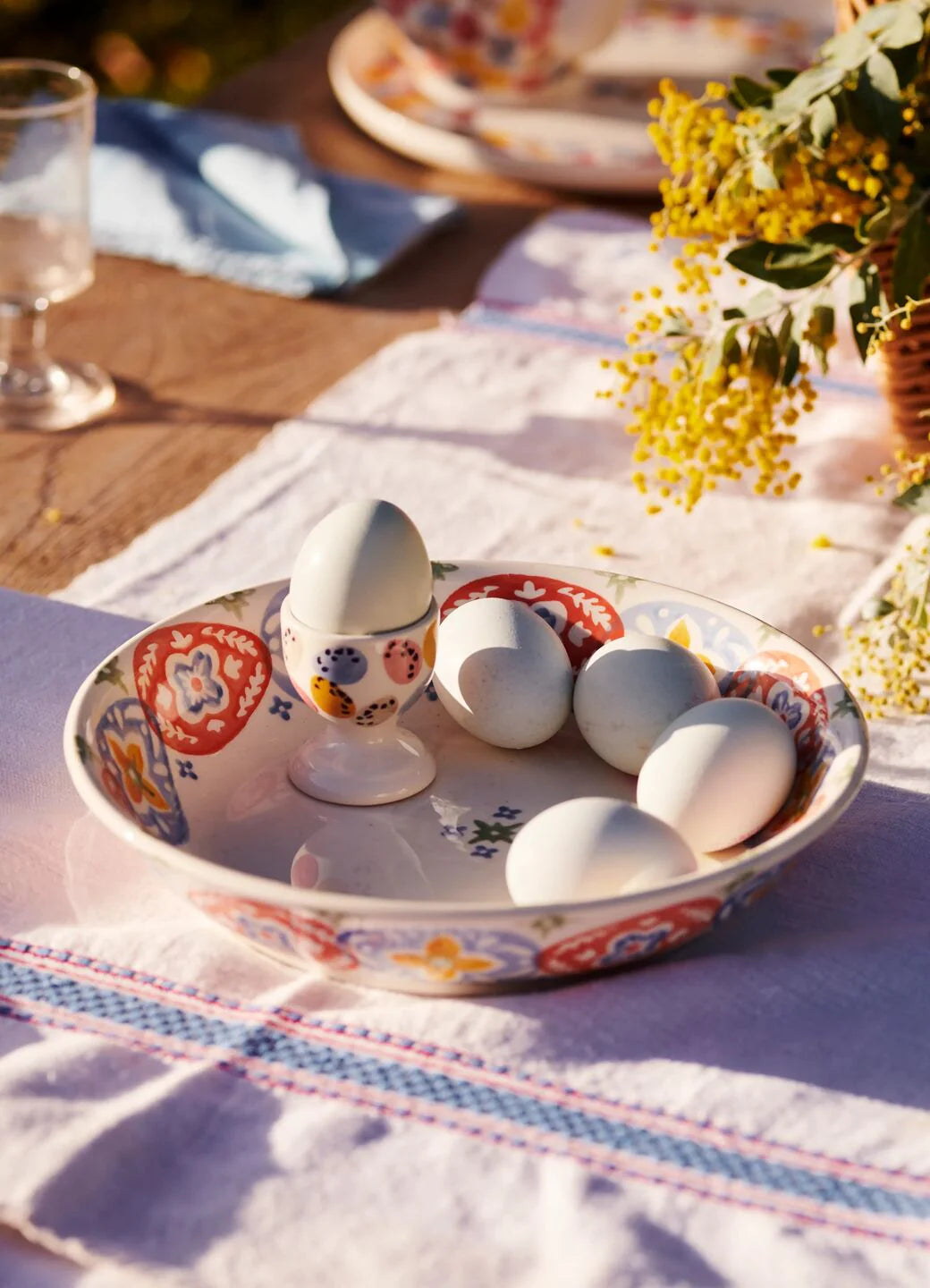 Decorative plate with eggs on a tablecloth with flowers and glasses in the background