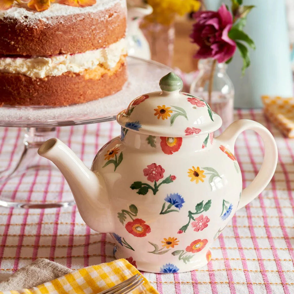 Floral teapot on a checkered tablecloth with a cake and flowers in the background