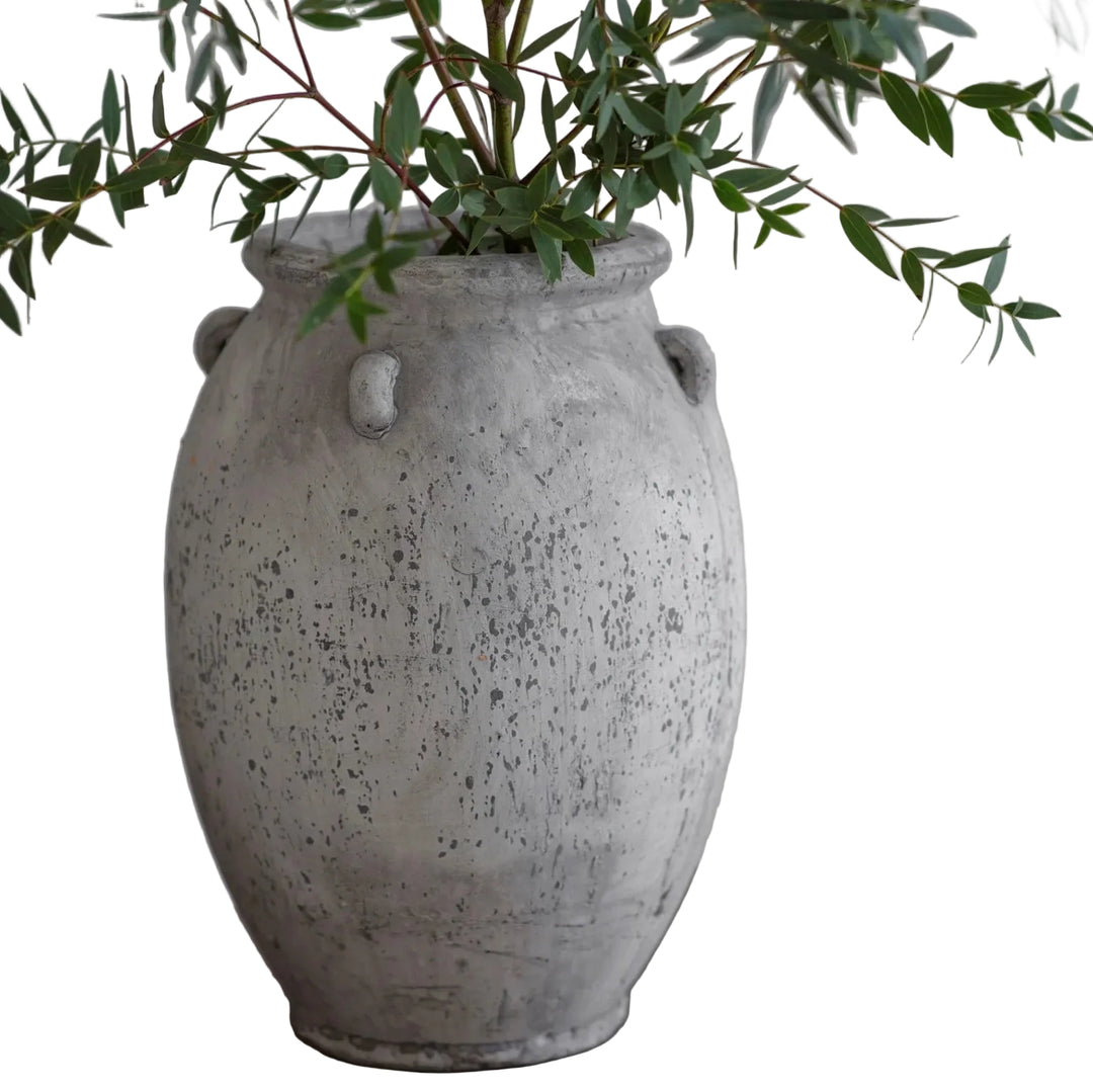 Speckled gray vase with green leaves on a neutral background