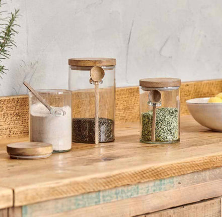 Three glass jars with wooden lids on a wooden surface, containing different items.