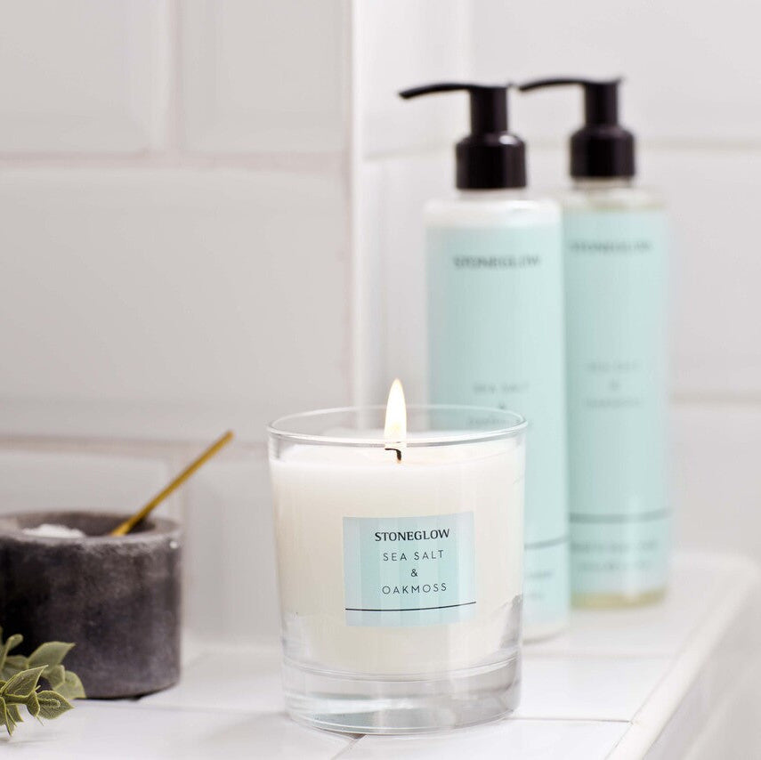 Candle and two bottles on a bathroom shelf with a tiled wall background
