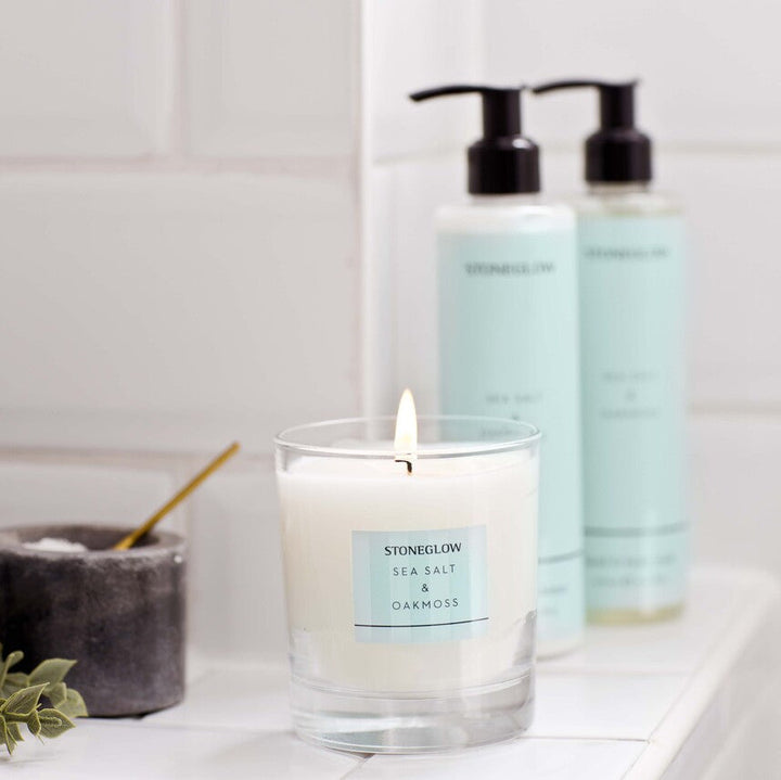 Candle and two bottles on a bathroom shelf with a tiled wall background