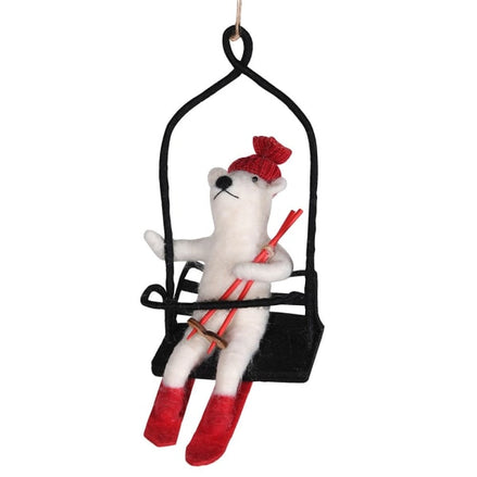 Decorative ornament of a polar bear on a ski lift with skis and a red hat.